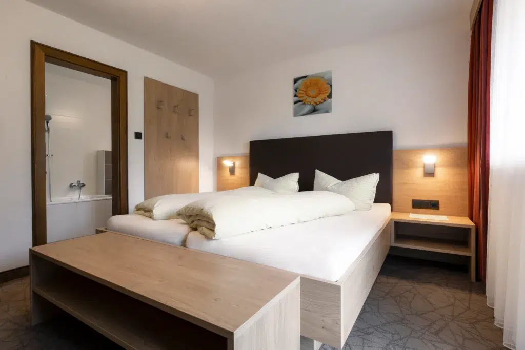 Modern eingerichtetes Doppelzimmer mit einem komfortablen Bett, Holzmöbeln und einem direkten Zugang zum Badezimmer.