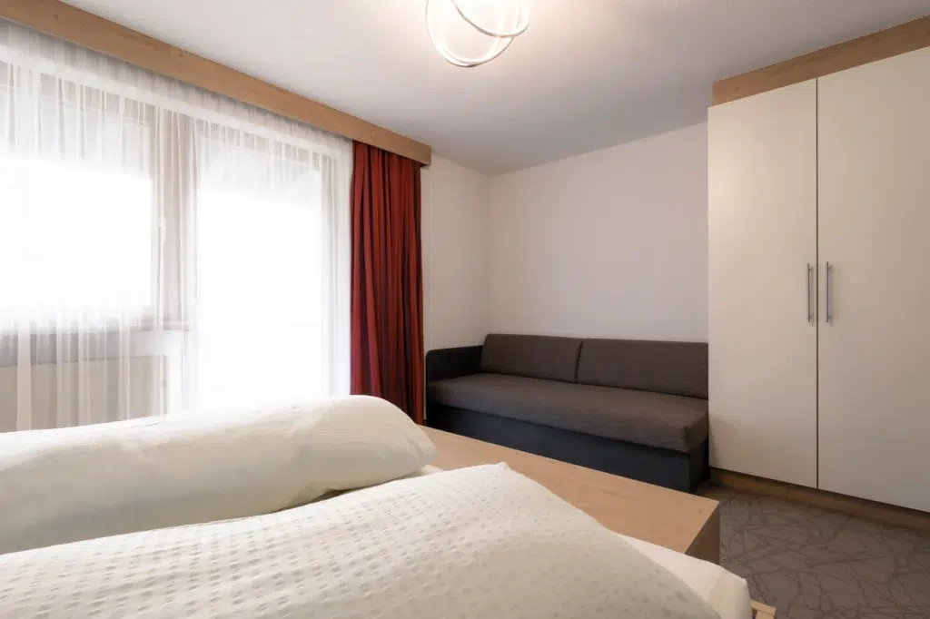 Stilvolles Schlafzimmer mit Doppelbett, einem gemütlichen Sofa und großen Fenstern mit viel Tageslicht und Vorhängen.