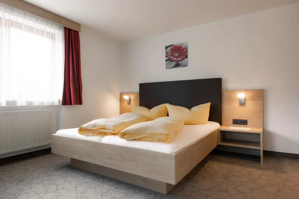Modern eingerichtetes Doppelzimmer mit einem komfortablen Bett, Holzmöbeln und einem direkten Zugang zum Badezimmer.